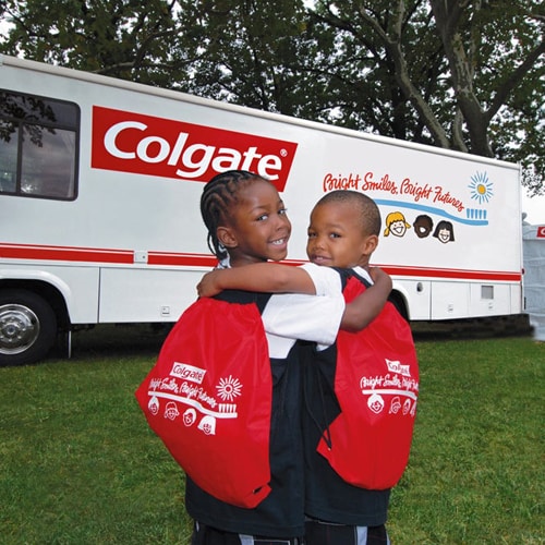niños pequeños sonríen frente a un camión de Colgate