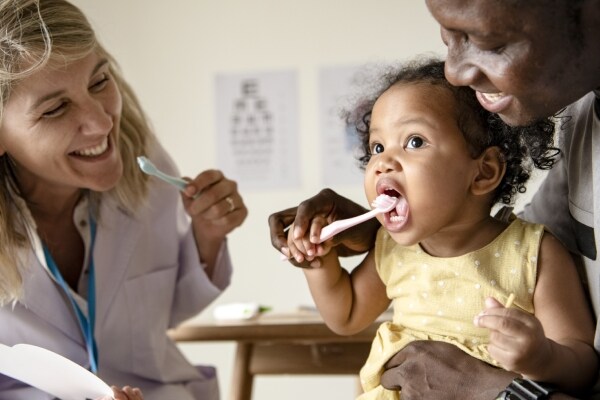 Doctora y padre enseñando a cepillar a niña