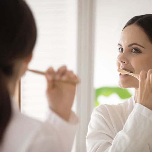 mujer joven en bata se cepilla los dientes