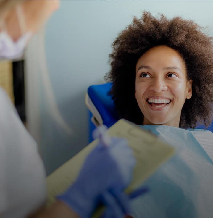 mujer con gran cabello rizado sentada en una silla de dentista y sonriendo