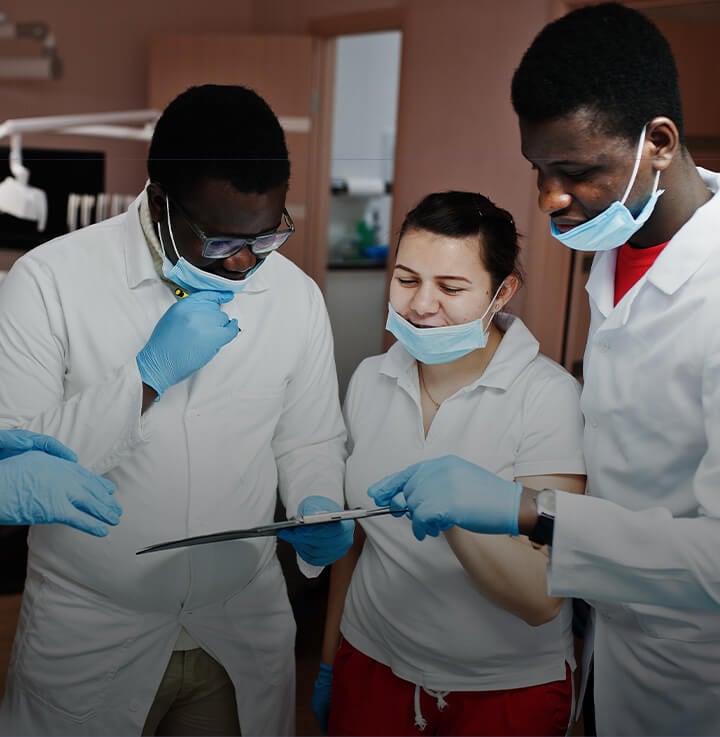 Equipo de 3 profesionales de la odontología con batas blancas mirando el historial de un paciente